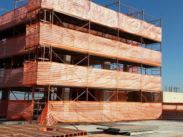 Edifício com andaimes e telas de proteção laranja.
